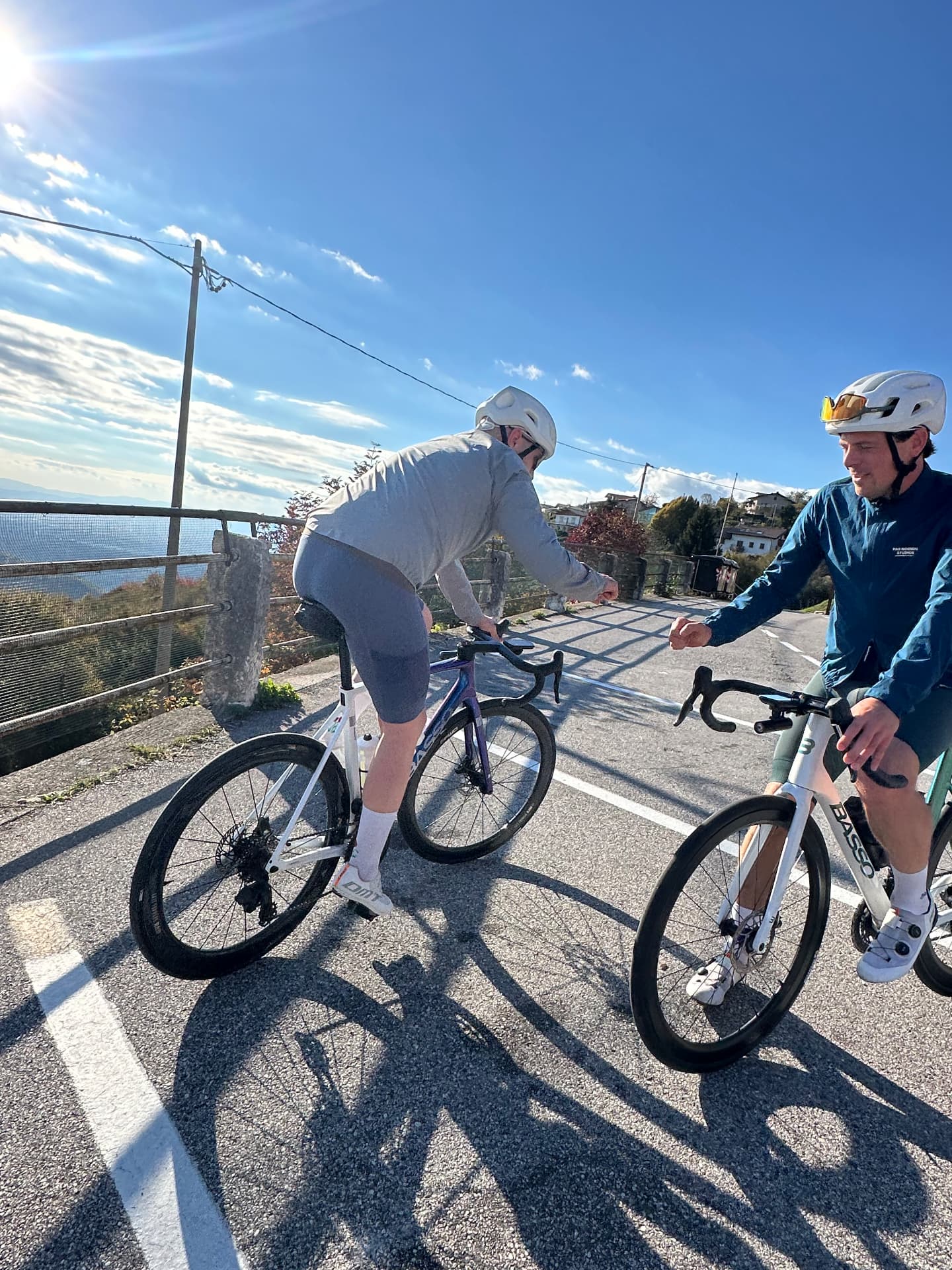 Twee renners op Basso racefietsen geven elkaar een vuist op een zonnige bergweg.